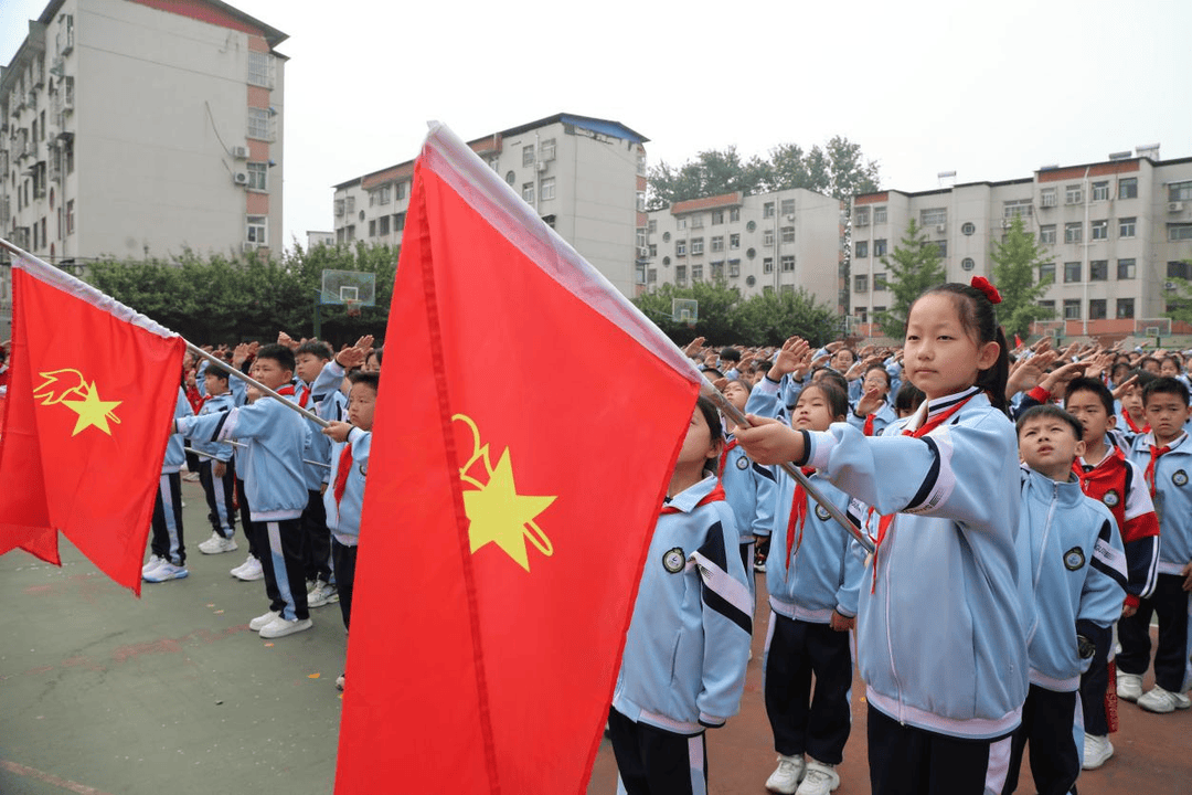 全体教师和一年级同学行注目礼,全体少先队员向着随风飘扬的五星红旗