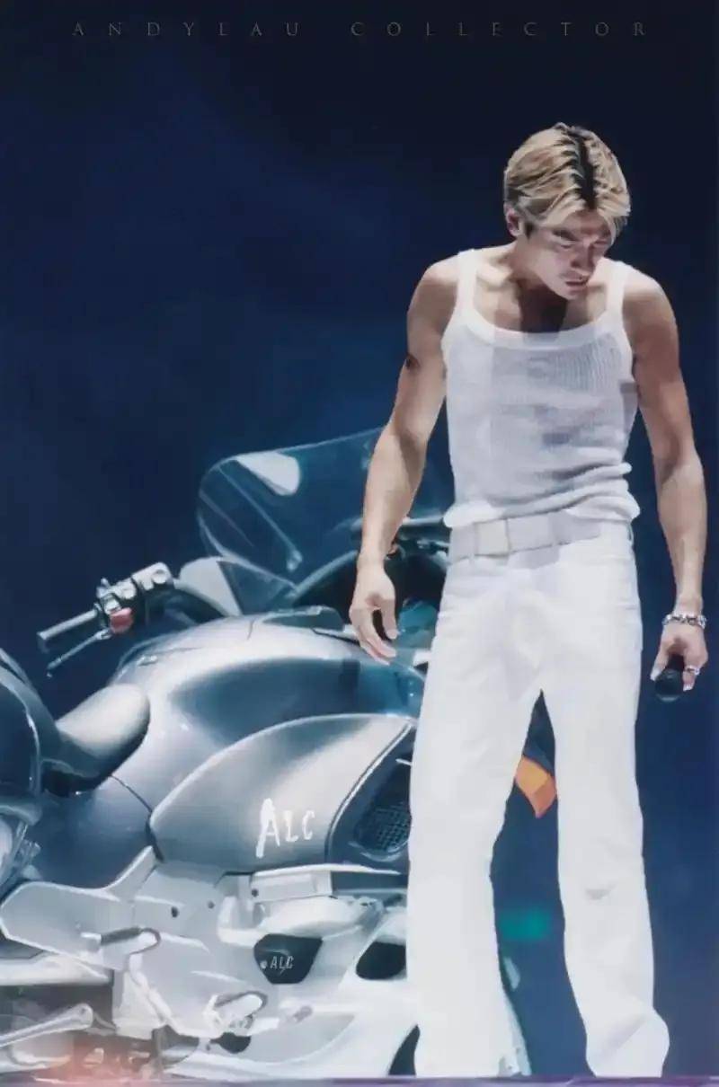 刘德华在摩托车上与舞伴进行暧昧互动,身着白背心,展现健美的肌肉线条