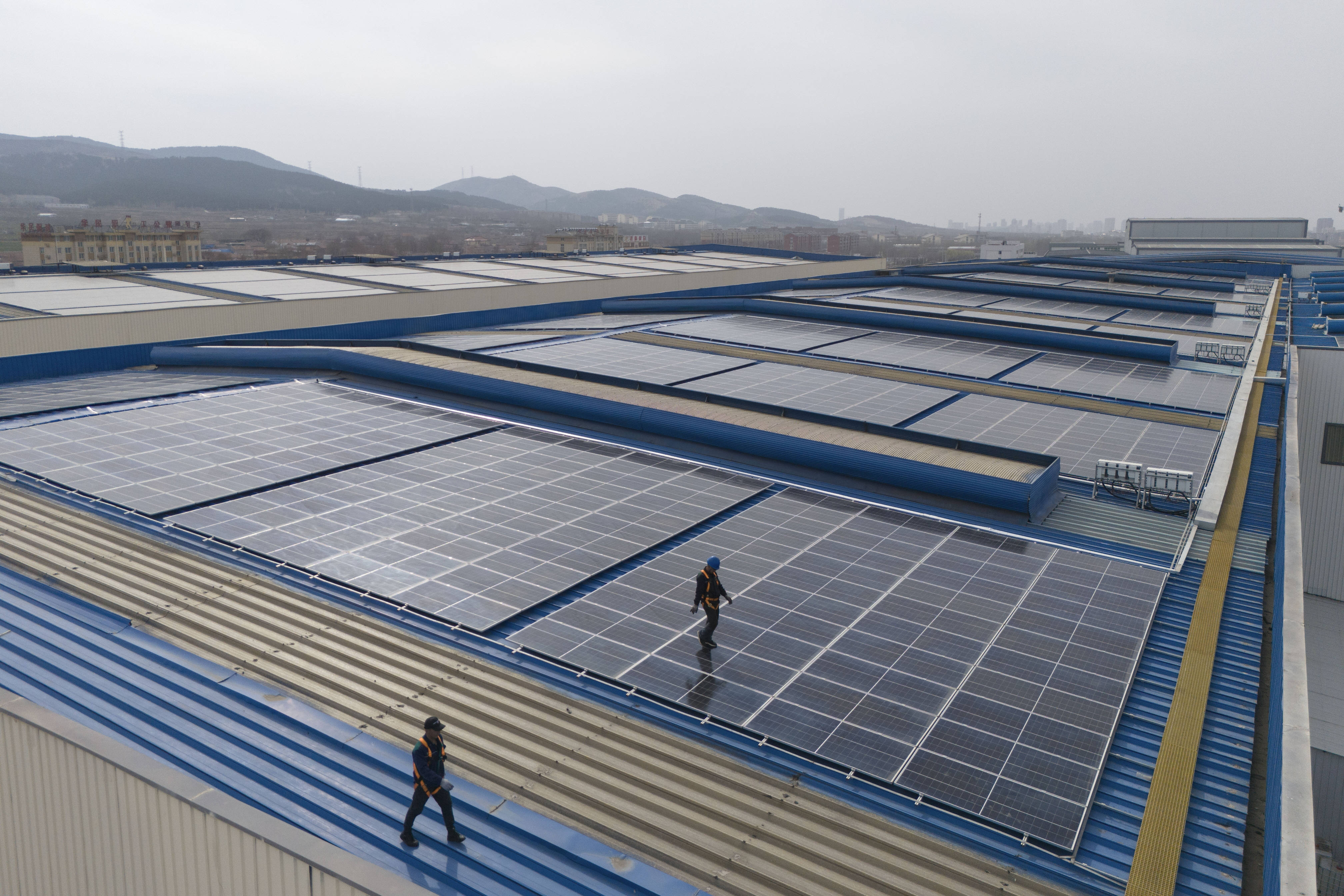 3月21日,工人们在山东省济南市郊区一座工厂的屋顶给太阳能电池板做